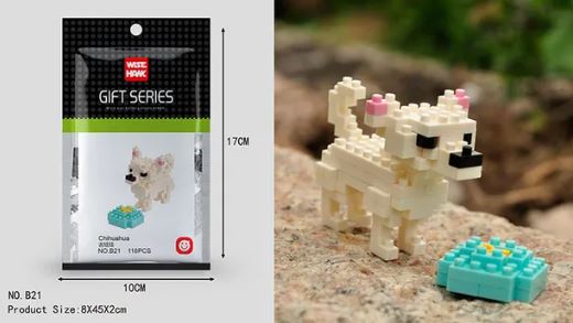 On a rocky surface, a small white pixelated dog toy from the Wisehawk set is next to a blue square object. Packaging on the left, labeled Gift Series with dimensions 17cm x 10cm, highlights this Mini Nano Micro Diamond Animal Building Blocks toy, ideal for fans of tiny building challenges.