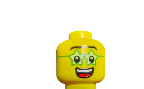 A LEGO 6294697 Minifigure Head features a beaming smile with green star-shaped glasses, wide-open eyes, and a red mouth on a crisp white background.