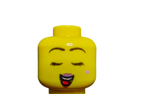The LEGO Minifigure Head (UB1490) features a cheerful face with closed eyes, pink lipstick, expressive eyebrows and eyelashes, and a charming small pink heart on one cheek.