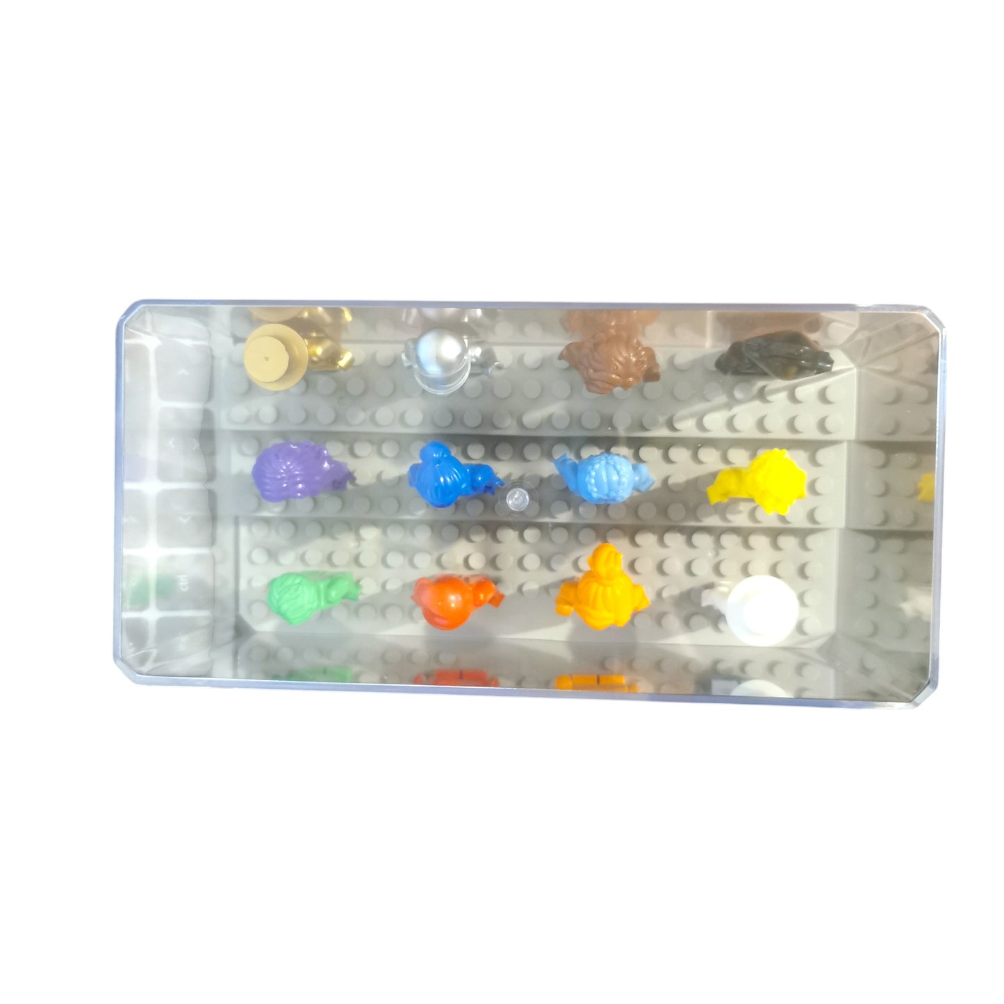 A transparent case holds 12 vibrant Colour Minifigures shaped like animals and objects on a pegboard surface. These eye-catching figures in bright yellow, orange, blue, and more create a striking visual against the reflective box surface.