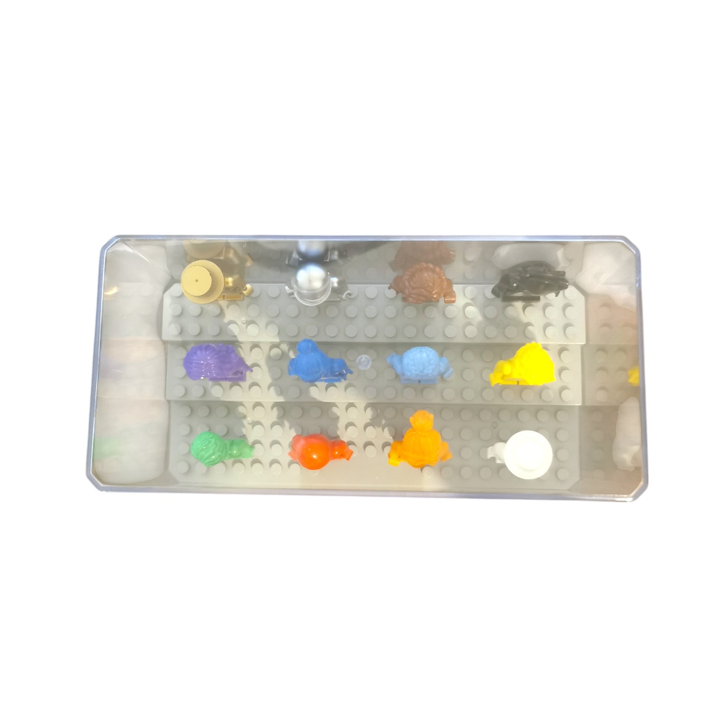 A transparent display case houses the Vibrant Colour Minifigures with Display Case, showcasing 12 eye-catching figures, including turtles, a snail, and other creatures in shades of purple, orange, green, yellow, blue, and white on a gray base.