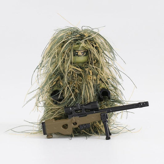 The Custom LEGO Minifigure Sniper, camouflaged in a green and brown ghillie suit, holds a toy rifle. Its face is partially hidden behind dark glasses on a plain white backdrop.