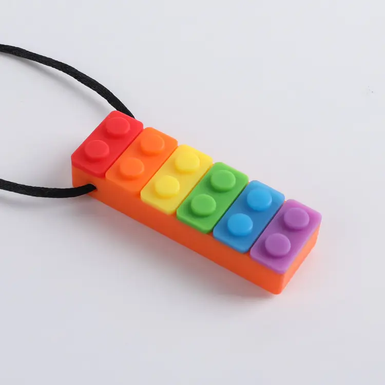 The Sensory Chew Necklace is a stack-inspired pendant in rainbow colors—red, orange, yellow, green, blue, and purple—on a black cord. Made of food-grade safety silicone, it aids autistic children and those with ADHD or anxiety.