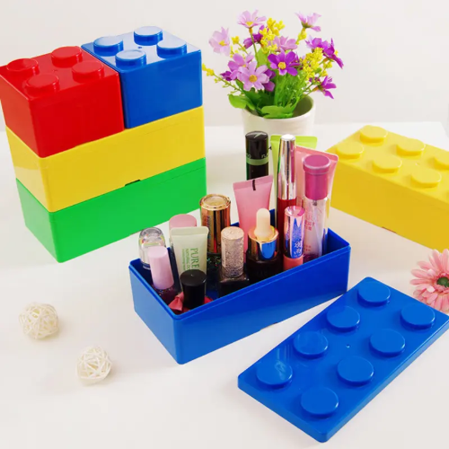 The Pack of 4 2x4 Storage Blocks in red, yellow, blue, and green neatly organize cosmetics like interlocking pieces. A small potted plant with purple flowers and decorative balls adds a charming backdrop.