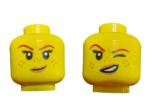 The LEGO 6223923 Minifigure Head features two yellow faces: one with spots, a raised eyebrow, and cheeky smirk; the other with a wink and wide grin. Both have freckles and cartoon-like expressions.