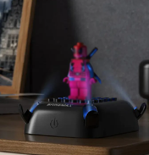 A pink and blue mini figure is placed on the 10 Color Changing Lighting Base for Minifigures, featuring touch controls for color changes and glowing blue accents, set on a wooden surface with a partial framed poster backdrop.