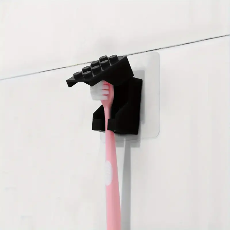 A pink toothbrush is held by a Kids Childrens Toothbrush Holder Wall-Mounted Brick Blocks Style, made from sturdy plastic, and mounted on a white tiled wall.