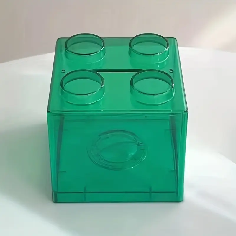 The Building Block Piggy Bank is a large, translucent green plastic storage box with four circular studs on top. Perfect for storing spare change, it cleverly resembles a toy building block and invites fun saving!.