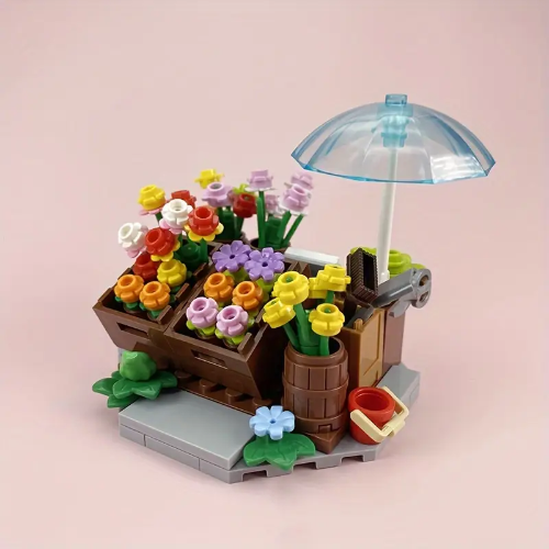 The Minifigure Flower Cart Plant Bouquet Building Blocks Set features vibrant flowers in yellow, purple, and red. It includes a transparent umbrella, wooden crate, and brown barrel on a gray base. Perfect for budding builders aged 6+, this set is an educational and creative gift.