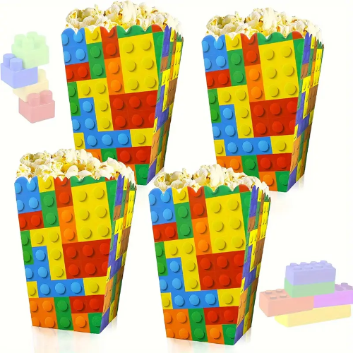 Four themed building blocks popcorn boxes designed for parties and game nights feature colorful, interlocking patterns like toy bricks, each filled with popcorn and some toy blocks are scattered nearby.