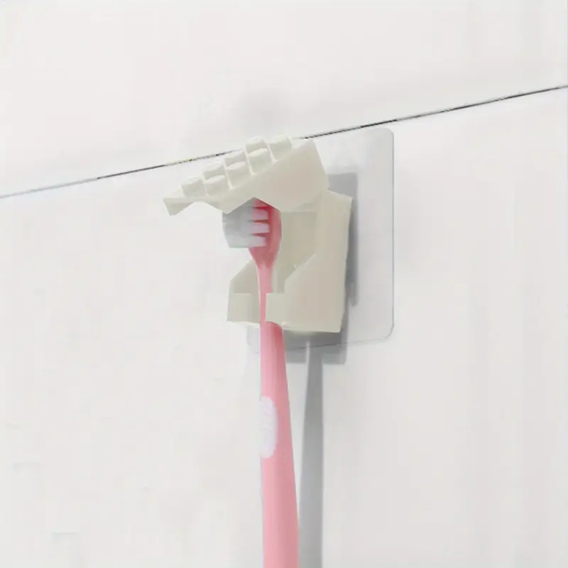 A durable plastic, fist-shaped holder securely grips a pink toothbrush between its thumb and fingers. Its vibrant hue reflects off the wall-mounted, dustproof design of this Kids Childrens Toothbrush Holder with a Brick Blocks Style.