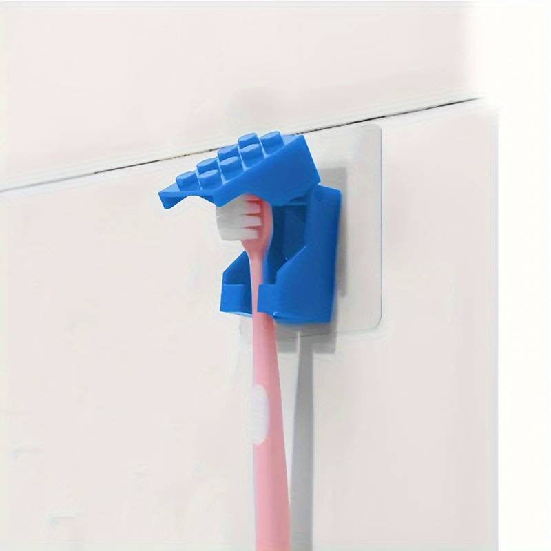 A pink toothbrush sits in a blue, wall-mounted Kids Childrens Toothbrush Holder designed like brick blocks, crafted from durable plastic. The bristles face outward as it securely attaches to a white tiled wall.